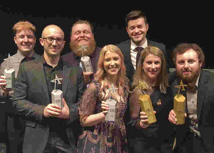 Photo of group at awards show holding gold and silver trophies 