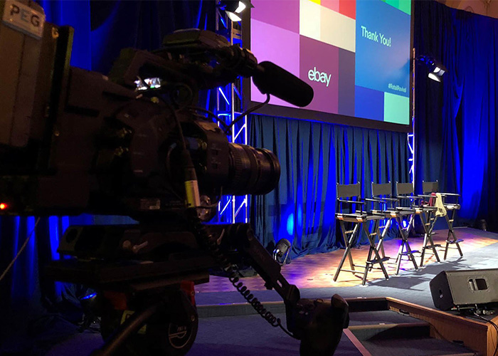 Live events camera in the shadows focused on 4 empty chairs on stage with eBay graphics behind them