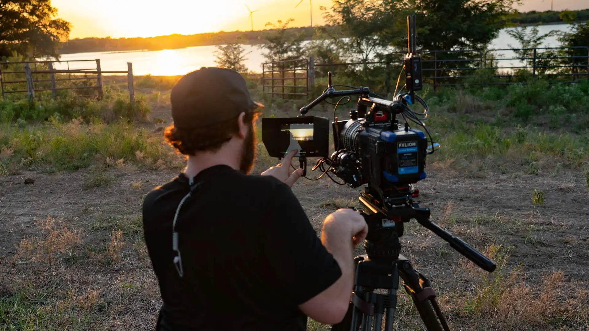 Pritt Entertainment Group Services, man kneeling on the ground outside next to camera capturing a sunset across lake 