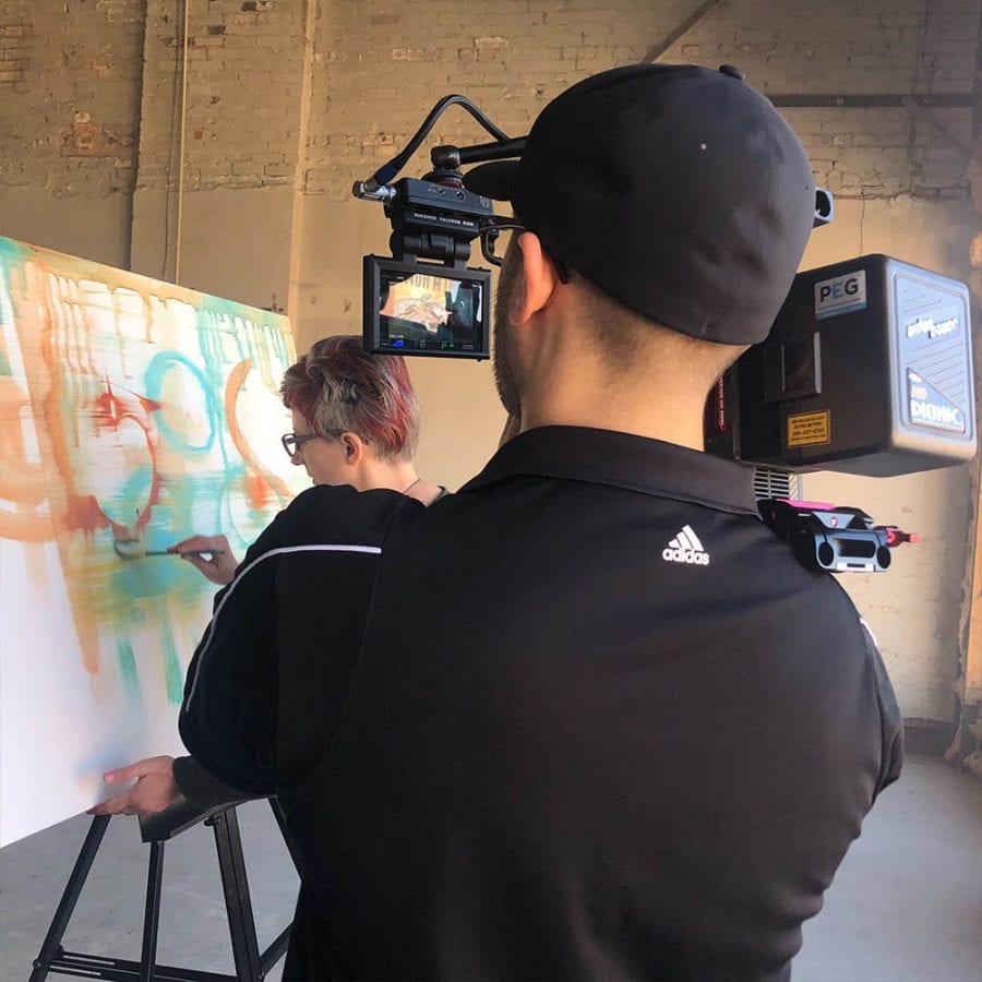 Over the shoulder shot of man filming a woman painting on a canvas 