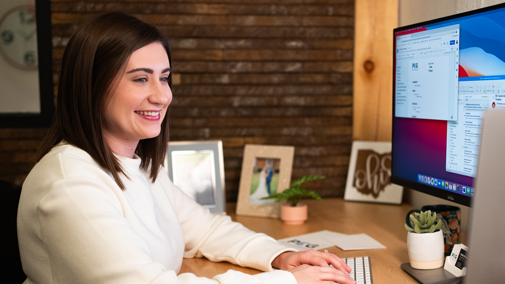 Woman smiling and looking at a computer monitor at modern wooden desk